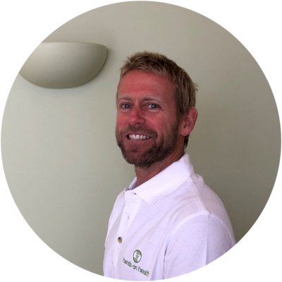 Dave Evans, wearing a white Hands-on Health branded polo shirt, smiling at the camera