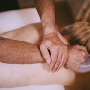 Massage therapist applies pressure to a patient's back by placing one hand over the other arm