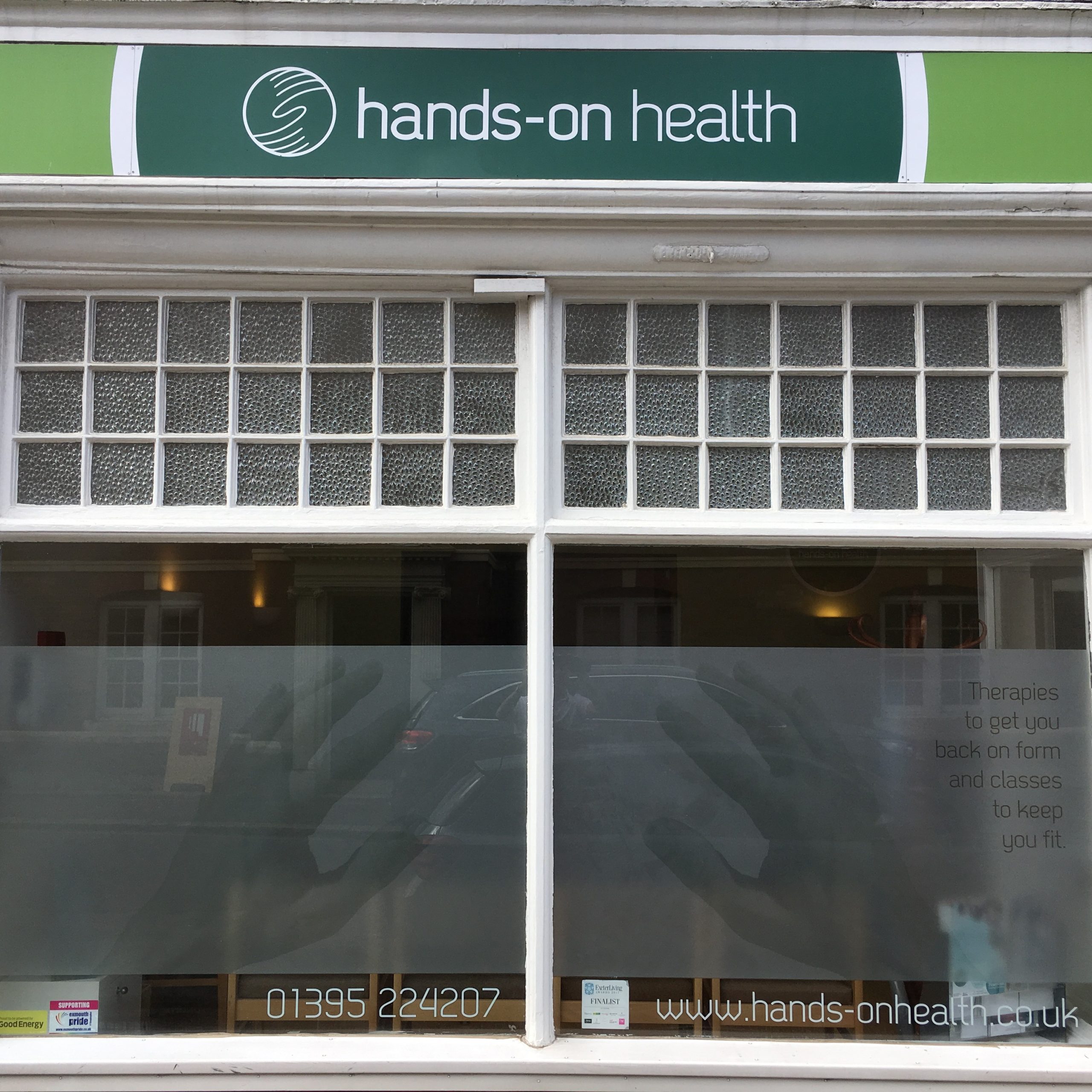 exterior-view-health-clinic-Exmouth.jpg Exterior view of the clinic, showing the logo above and contact details with an image of hands on the window film
