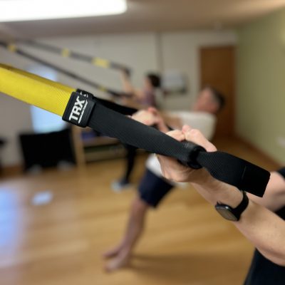 Close-up of TRX strap being held at an angle. Two people also holding TRX straps in out-of-focus background.