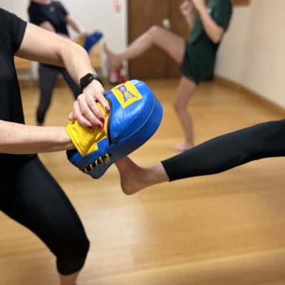 kickboxing-exmouth.jpg One figure holds a focus pad while another kicks it. Two people can be seen out of focus in the background doing the same move.