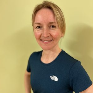 Maria smiling at the camera, with her blonde hair tied back and wearing a navy t-shirt with a white logo